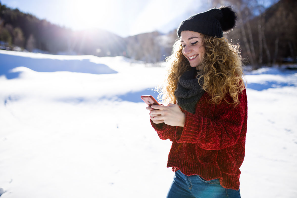 Woman smiling while planning a winter trip on her phone, showing how agentic commerce in travel simplifies booking.